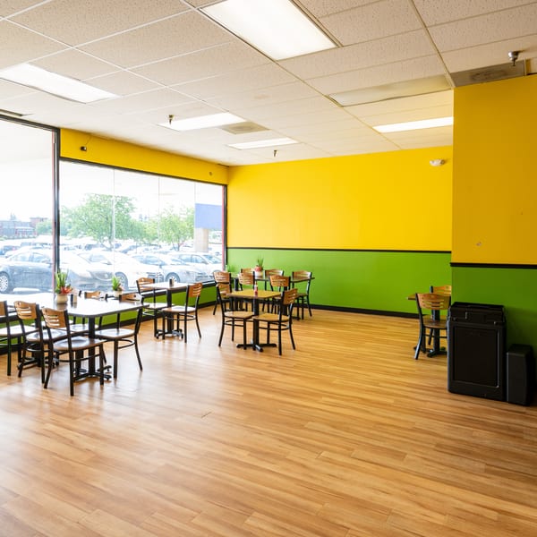Empty restaurant dining room with bright yellow and green walls, wooden floors, and tables by large windows.