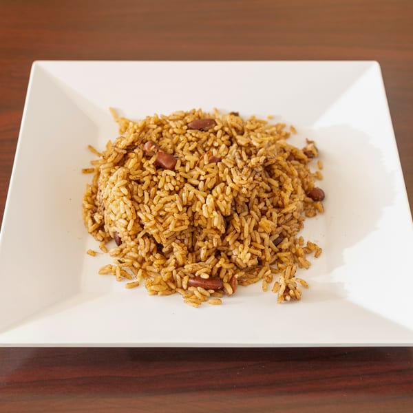 A white square plate filled with seasoned rice and kidney beans on a wooden table.