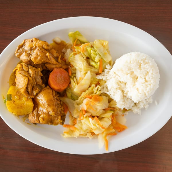 Curry chicken with potatoes and carrots, steamed cabbage, and white rice on a white plate.