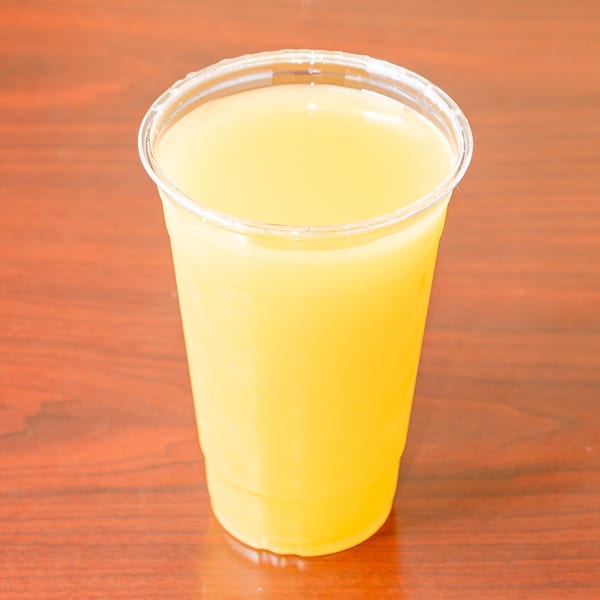 A clear plastic cup filled with bright yellow juice sits on a dark wooden table.