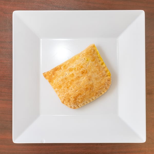 Golden brown Jamaican beef patty on a white square plate, centered on a wooden table.