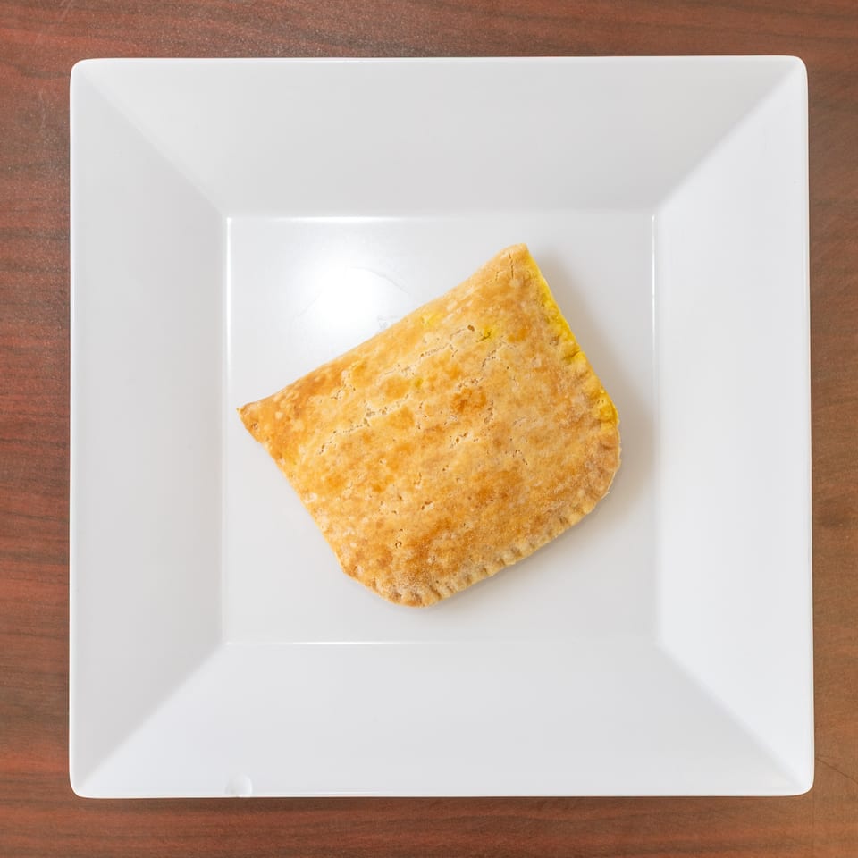 Golden brown Jamaican beef patty on a white square plate, centered on a wooden table.