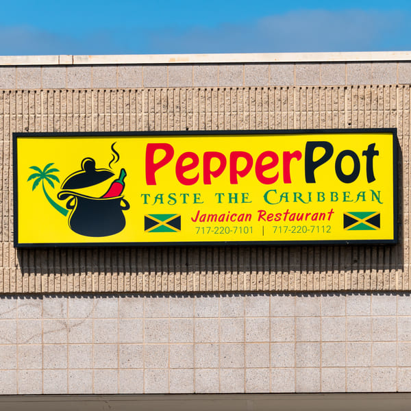 Bright yellow PepperPot Jamaican Restaurant sign with a cooking pot, chili, and palm tree logo.