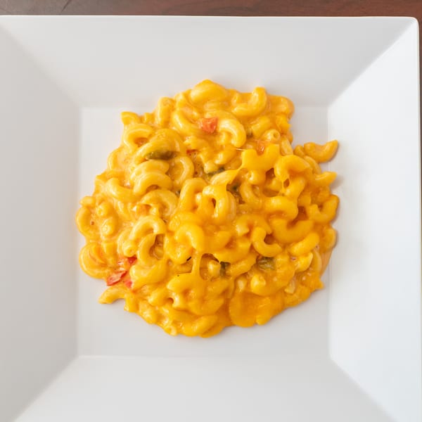 Creamy macaroni and cheese with red and green peppers on a white square plate.