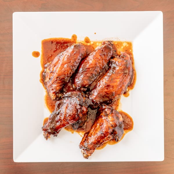 Five glazed chicken wings covered in a rich, dark sauce on a white square plate.