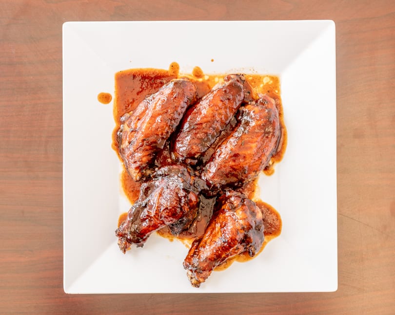 Five glazed chicken wings covered in a rich, dark sauce on a white square plate.