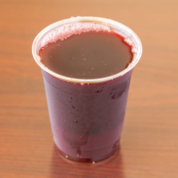 A clear plastic cup filled with a dark red beverage, possibly juice, on a wooden surface.
